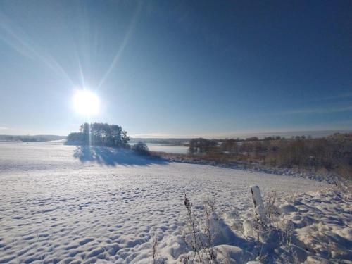 a snow covered field with the sun in the background at Między Olchami domek nad jeziorem. Noclegi całoroczne. Cisza, spokój. in Barczewo