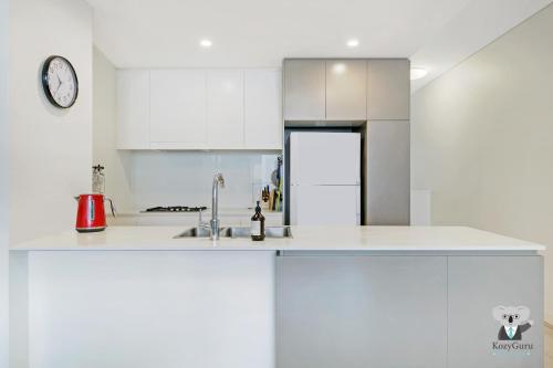 a white kitchen with a sink and a clock at KOZYGURU MASCOT 2 BED APT FREE DOUBLE-PARKING NMA629 in Sydney