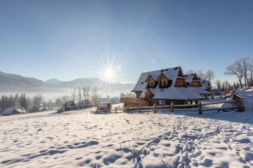 a house covered in snow with the sun in the background at udanypobyt Tatrzańskie Domy in Kościelisko