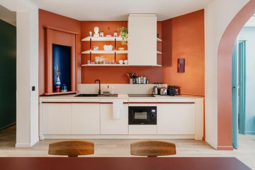 a kitchen with white cabinets and an orange wall at Edgar Suites Auteuil - Le Marois in Paris