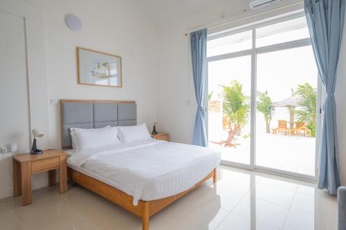 a white bedroom with a bed and a large window at True South in Maradhoofeydhoo