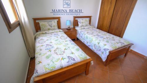 sypialnia z dwoma łóżkami i znakiem, który oznacza ubezpieczenie plaży kamakura w obiekcie Marina Beach Appart Hôtel w mieście Mʼdik