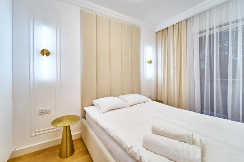 een witte slaapkamer met een bed en een kruk bij LAGUNA Apartament Polanica Residence 20 in Polanica-Zdrój