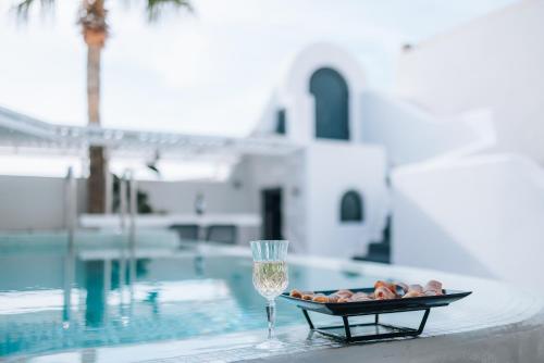 a plate of food and a glass of wine next to a swimming pool at Opera Mansion Santorini in Fira