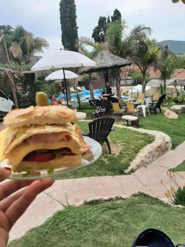 uma pessoa segurando um prato com uma sanduíche sobre ele em Complejo Los Cipreses em Villa Carlos Paz