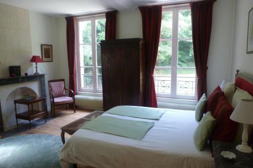a bedroom with a bed and a fireplace and windows at Chambres d'Hôtes Le Bas Manoir in Bretteville-sur-Odon