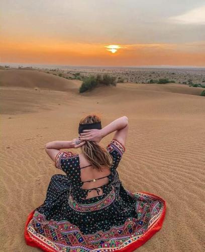 a woman sitting in the desert watching the sunset at Mirvana Guest House & Camel safari in Jaisalmer