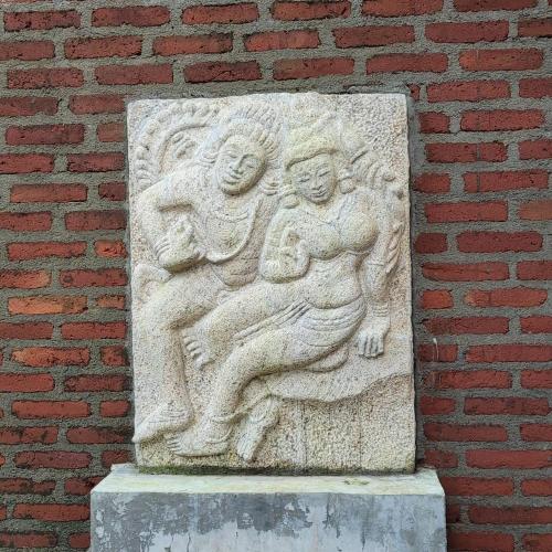 a stone statue of two people on a brick wall at Arachchi Heritage in Anuradhapura