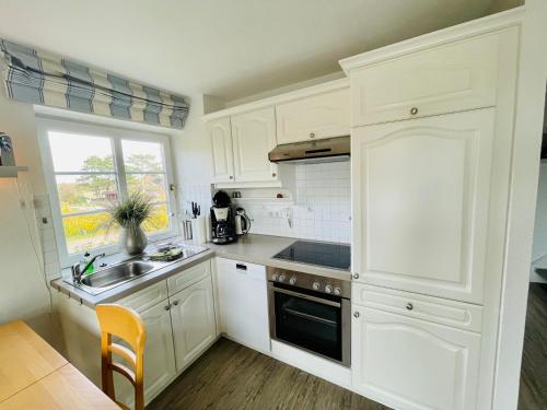 Una cocina con gabinetes blancos y un fregadero y una ventana. en Ruheoase am Dorfteich für 2-4 Personen, en Wenningstedt