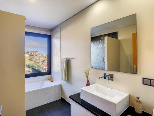 een badkamer met een wastafel, een bad en een spiegel bij Villa Serramar in Estreito da Calheta