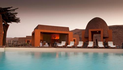 a resort with a pool with chairs and a building at Okahirongo Elephant Lodge in Purros