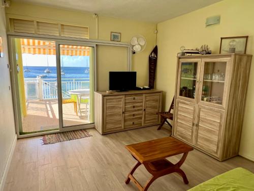 a living room with a television and a balcony with the ocean at Ti Cabanon. Appartement vue mer à Deshaies. in Deshaies