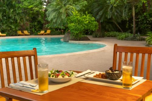 a table with a plate of food next to a pool at Capitán Suizo Beachfront Boutique Hotel in Tamarindo