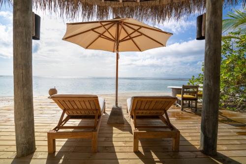 a patio with two chairs and an umbrella on the beach at Six Senses Laamu in Laamu