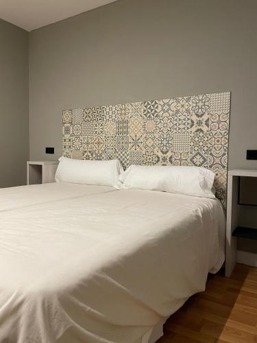 a bedroom with a large white bed with a headboard at Pensión Belmonte - check in Hotel a 650 metros in Gijón