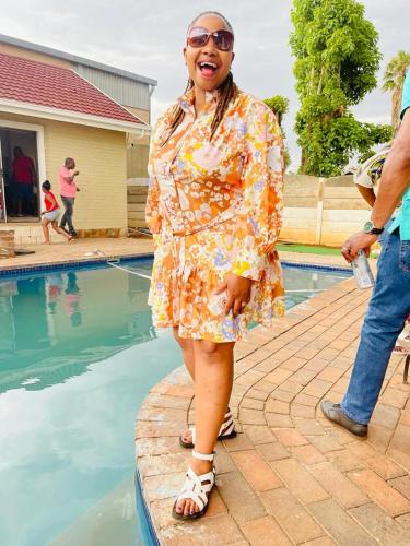 a woman in a dress standing next to a swimming pool at CapitalT Luxury Guest House in Germiston