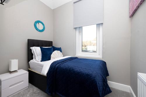 a bedroom with a bed with a blue comforter and a window at Stylish George Street Apartment in Peebles