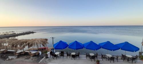 a group of tables and blue umbrellas on the beach at San Georgio Hotel in Tsoutsouros