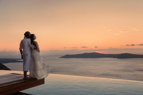 a man and a woman standing on the edge of a pool at West East Suites in Imerovigli