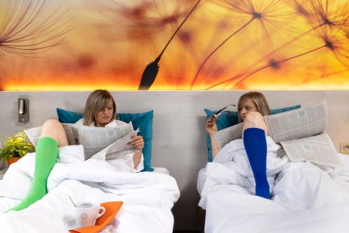 two women laying in bed reading books and reading newspapers at Logis Hôtel-Restaurant LE FONTARABIE in Fontenay-le-Comte