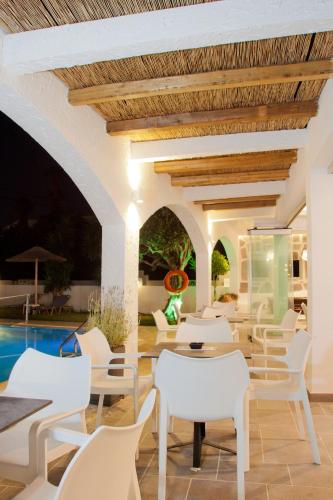 a patio with white chairs and tables and a pool at Malibu Boutique Studios & Bungalows in Faliraki