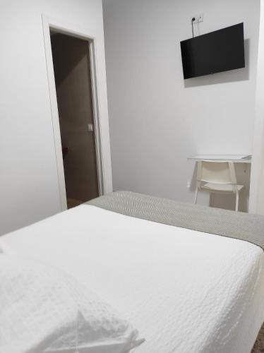Cama blanca en habitación blanca con silla en Hostal Mellizo en Lebrija