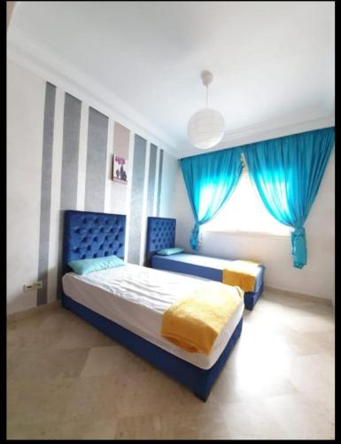 a bedroom with two beds with blue curtains and a window at Résidence jnane California in Casablanca