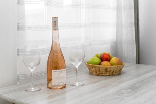 two wine glasses and a bottle and a basket of apples at Anius Apartments in Mýkonos City