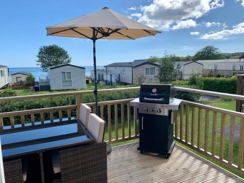 a grill on a deck with an umbrella and a laptop at Lydstep Beach BayView 3-Bedroom Holiday Home in Tenby