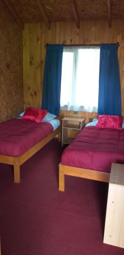 a bedroom with two beds and a window with blue curtains at Hospedaje Picoyo in Pucón