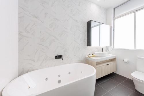 a white bathroom with a tub and a sink at Meriton Suites Bondi Junction in Sydney