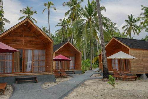 una fila de cabañas en la playa con palmeras en Pulau Mahitam Resort & Cottage by Hotelku en Ratai