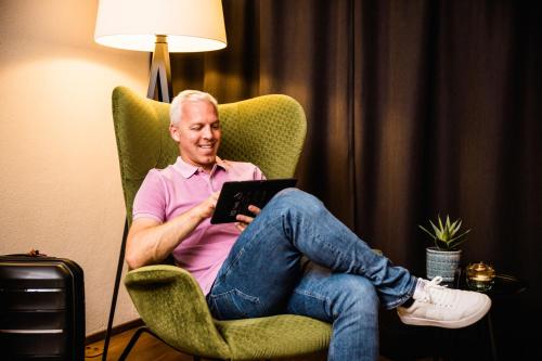 a man sitting in a chair with a tablet at Wirthshof Hotel & Chalets in Markdorf