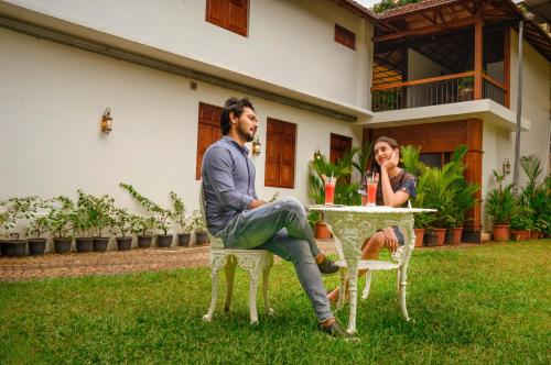 a man and woman sitting at a table in front of a house at Surya Heritage Hotels in Kannur