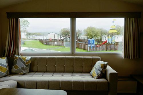a couch in a living room with a large window at Plot 188D Lakeside Cabin, Wyldecrest, Millom in Millom