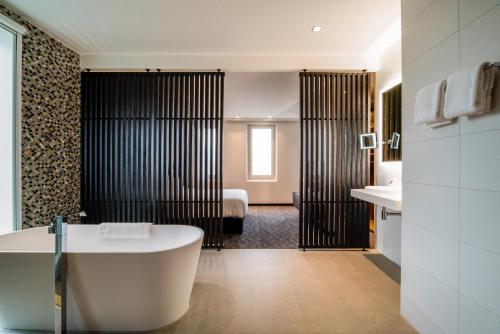 a bathroom with a bath tub and a bedroom at Radisson Hotel & Suites Amsterdam South in Amstelveen