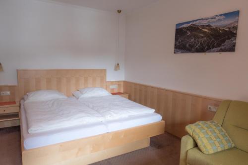 a bedroom with a white bed and a chair at Die Pension - Margreiter in Saalbach Hinterglemm