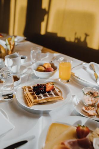 a table with waffles and a bowl of fruit and orange juice at Parkhotel Egerner Höfe in Rottach-Egern