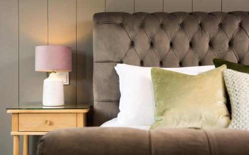 a bed with a gray headboard and a table with a lamp at Willowbeck Lodge Boutique Hotel in Carlisle