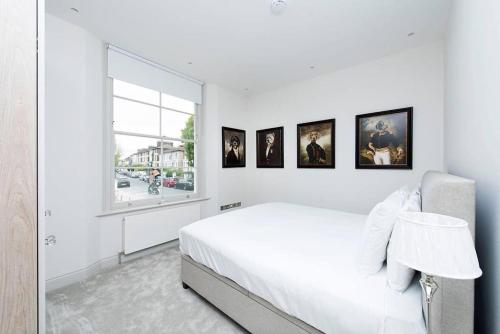 biała sypialnia z łóżkiem i obrazami na ścianie w obiekcie Recently redecorated bright 1BR near Shepherds Bush with parking SOA w Londynie