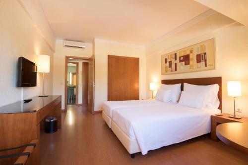 a hotel room with a white bed and a flat screen tv at Vila Gale Cerro Alagoa in Albufeira