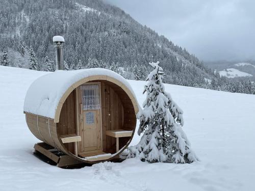 a wooden cabin in the snow with a snow covered tree at Moosgut in Abtenau