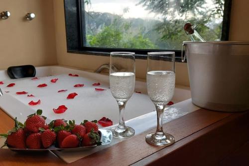 two wine glasses and a plate of strawberries on a counter at Casa do Alto Santa Mônica- Natureza ao seu redor in Itaipava