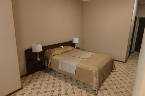 a small bedroom with a bed and two lamps at Medeu in Kostanay