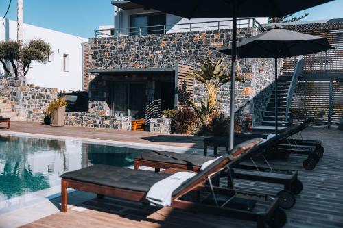 a swimming pool with an umbrella and benches next to a house at Seascape Luxury Residences in Agia Pelagia