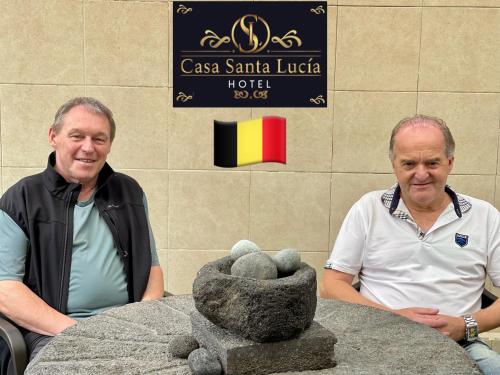 two men sitting next to a table with a statue at Hotel Casa Santa Lucía in Baños