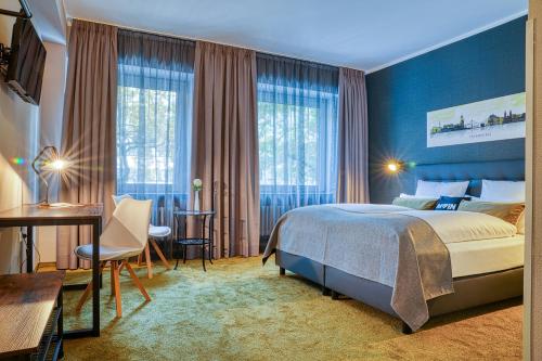 a bedroom with a bed and a desk and windows at Centro Hotel City Gate in Hamburg