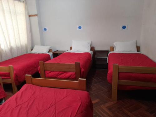 a room with three beds with red sheets and two chairs at Inka's Rest Hostel in Puno