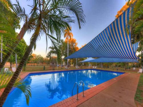 a swimming pool with a palm tree and a building at BIG4 Breeze Holiday Parks - Katherine in Katherine
