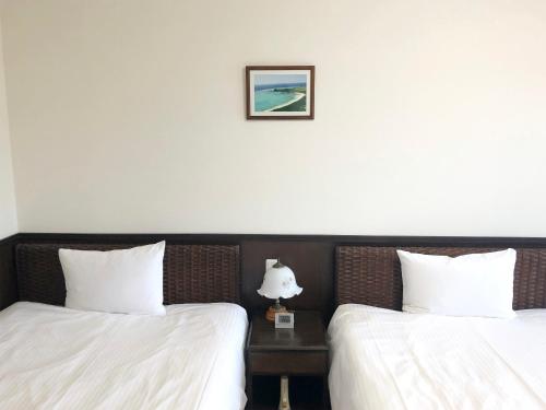 two beds with white sheets and a table with a lamp at Pine Shima Resort Coral Fish in Ibaruma